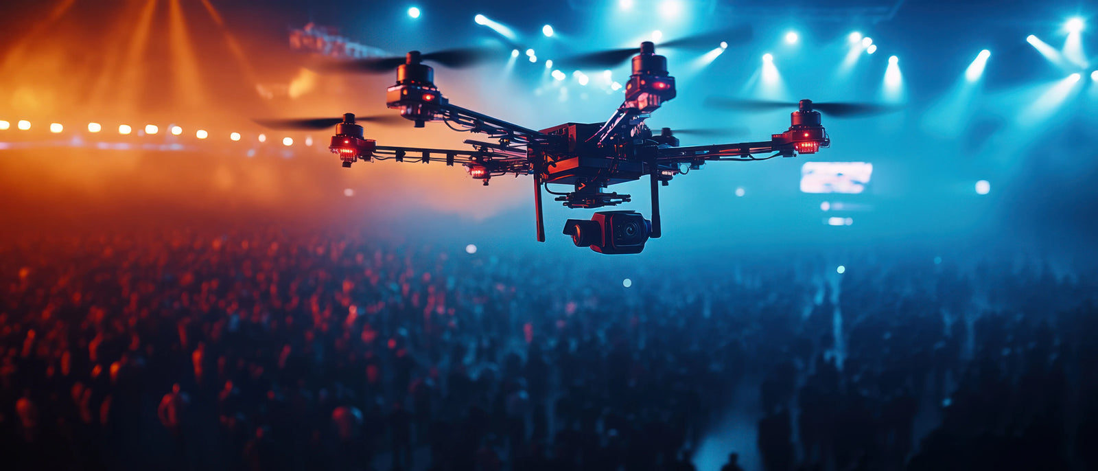 A camera drone suspended over a large concert crowd lit by blue and orange stage lights.