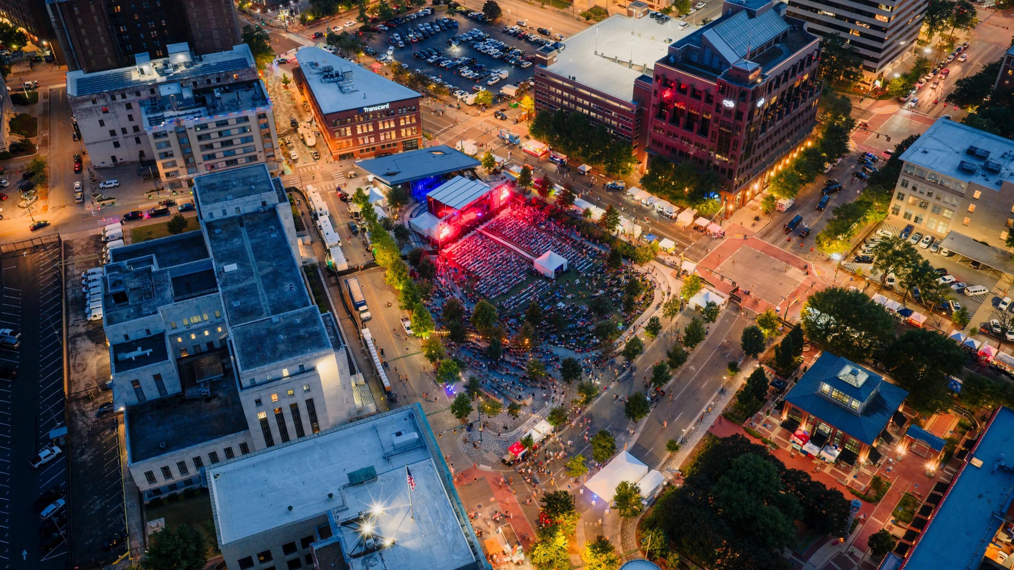Aerial night photograph of a large outdoor concert stage in a city plaza surrounded by lit buildings.