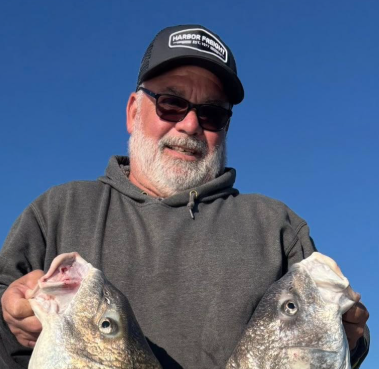 Cory Hart holding two fish against a clear blue sky.