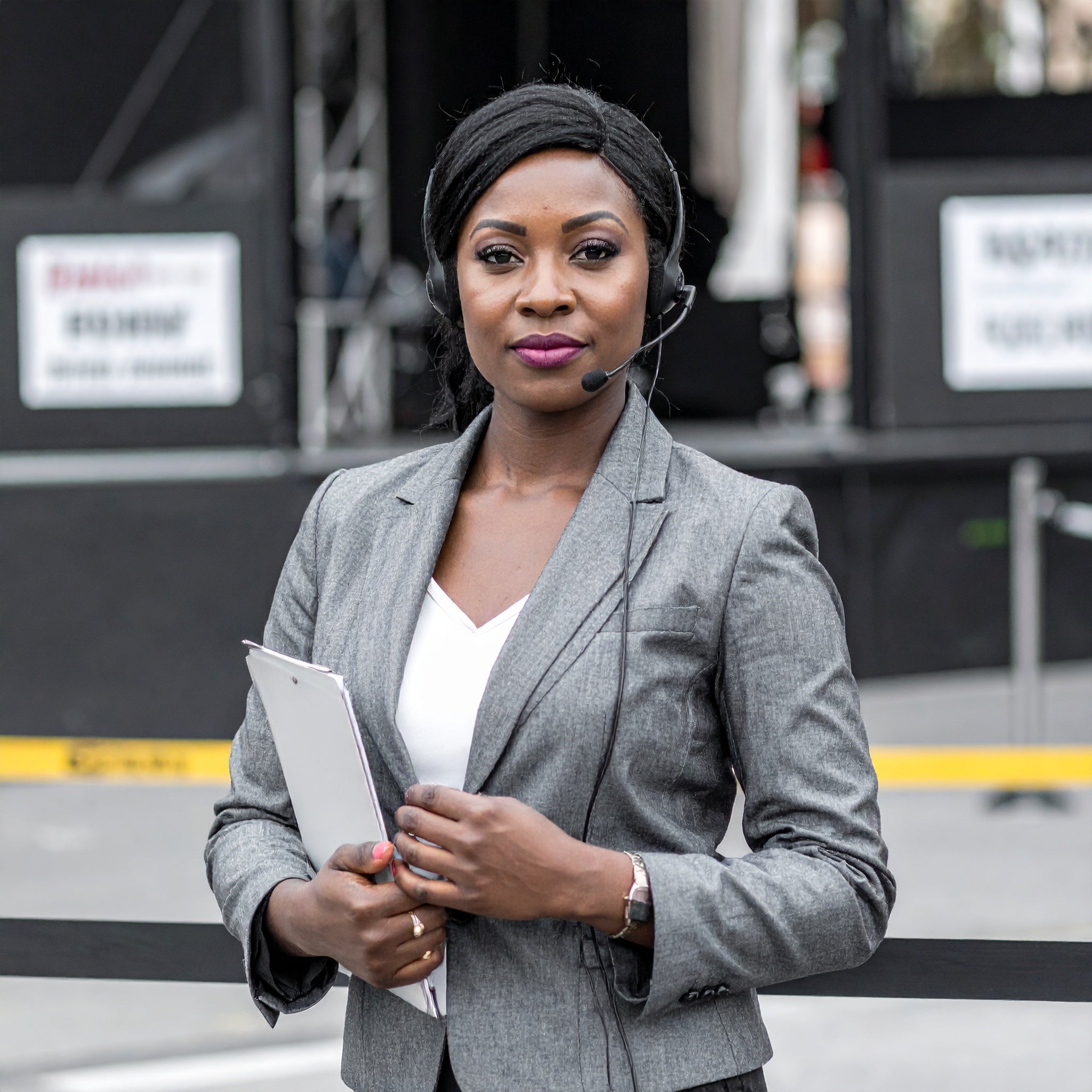 Woman in a gray blazer holding a tablet outdoors with equipment in the background