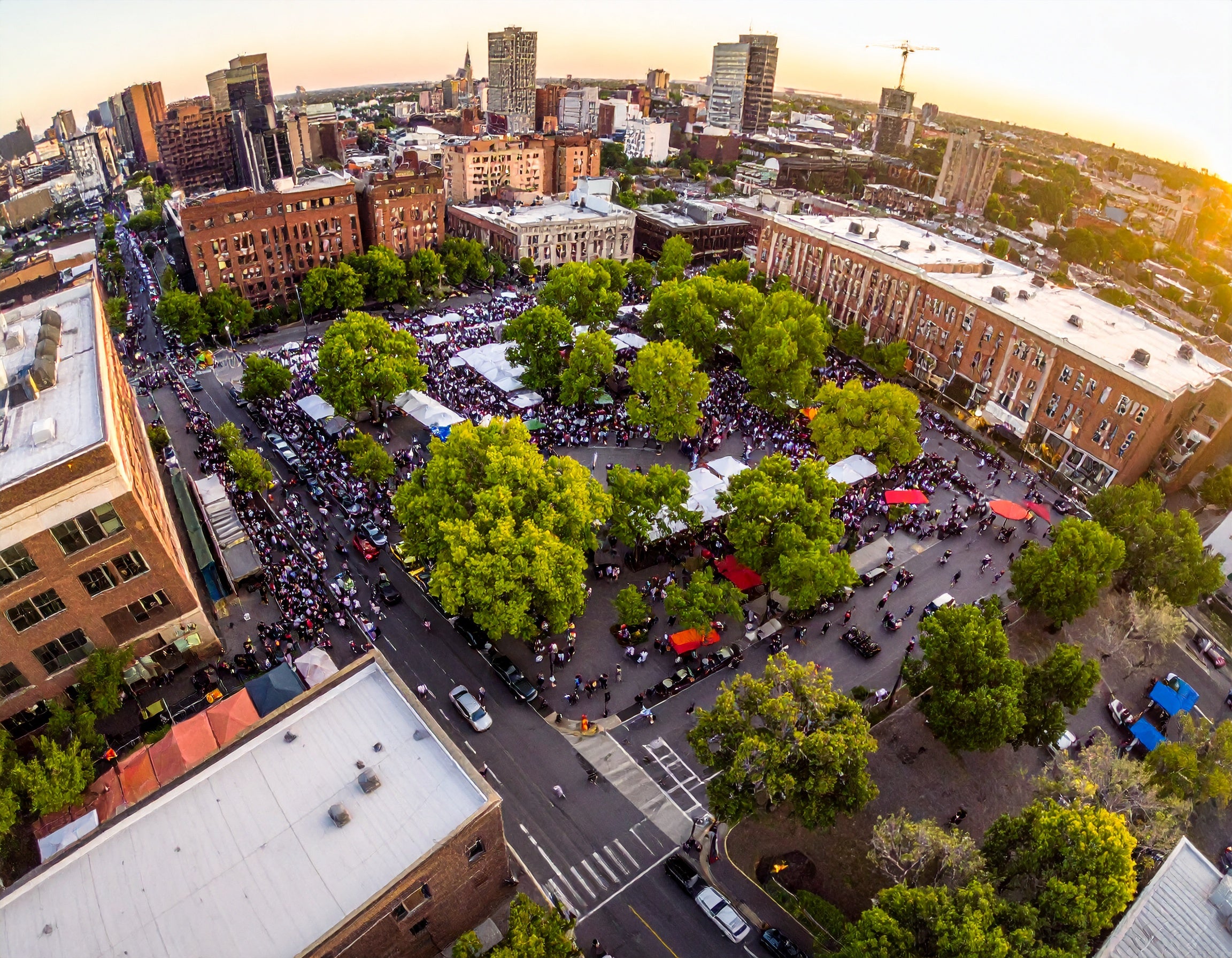 Aerial view of a city street with trees and people, during sunset.